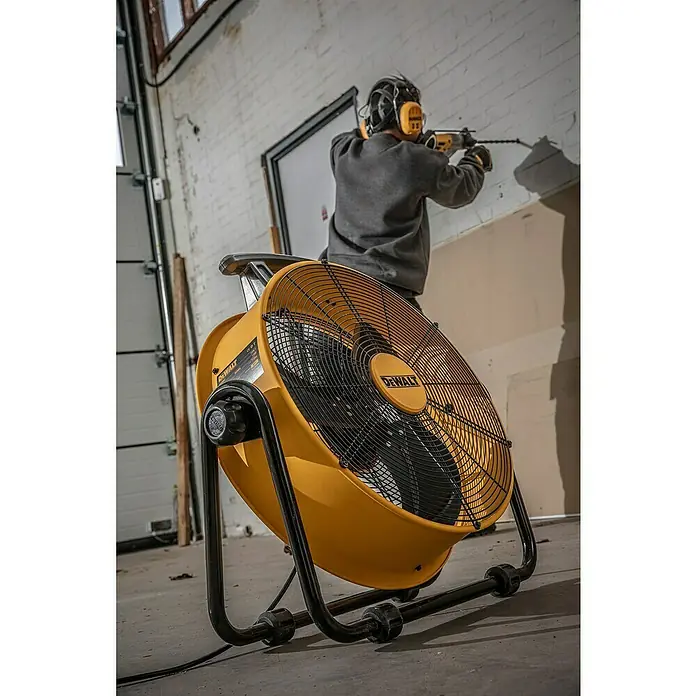DeWalt Bodenventilator DXF2067 - 110 W, Max. Luftleistung: 102,2 m³/h - Der DeWALT-Ventilator bietet starke Kühlung für Baustellen. Ein Bauarbeiter bohrt mit Gehörschutz ein Loch in eine Wand, die sich im Hintergrund befindet.