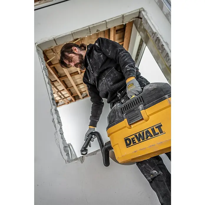 DeWalt Elektro-Nass- & Trockensauger DXV23G - 230 W, Behältervolumen: 23 l - Ein Mann benutzt einen gelben DEWALT Staubsauger, um Bauarbeiten zu reinigen. Er trägt dabei Handschuhe und eine schwarze Jacke.
