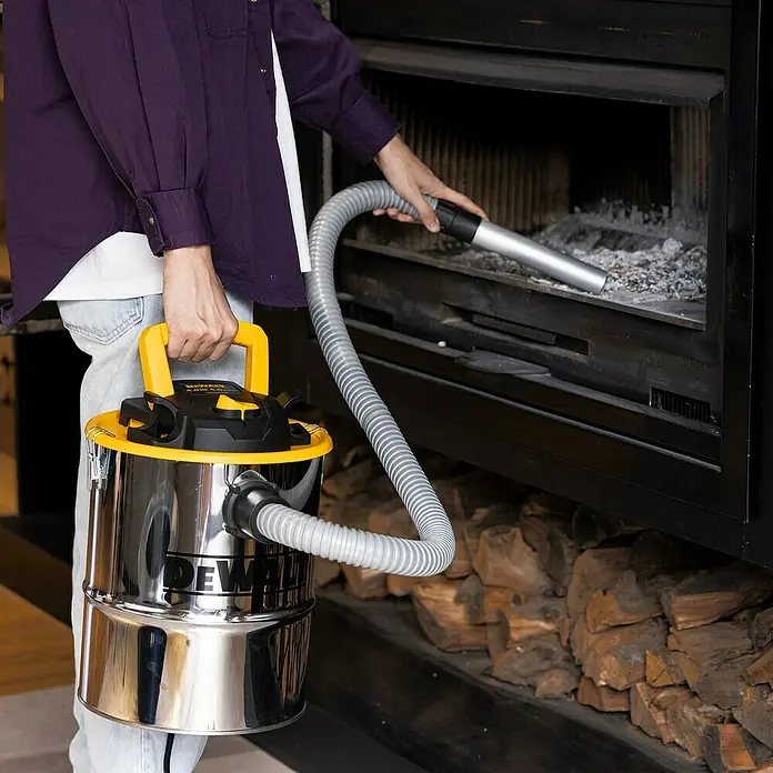 DeWalt Elektro-Aschesauger DXV15A - 600 W, Behältervolumen: 15 l, Mit Beutel - Eine Person reinigt einen Kamin mit einem chromfarbenen DeWalt Staubsauger mit gelben Akzenten, um Asche zu entfernen.