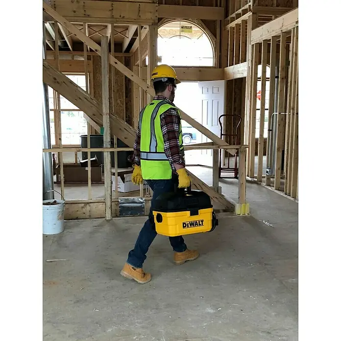 DeWalt Elektro-Nass- & Trockensauger DXV15T - 1.100 W, Behältervolumen: 15 l, Filterreinigung: Vollautomatisch - Bauarbeiter trägt einen gelben DeWalt Staubsauger auf einer Baustelle.