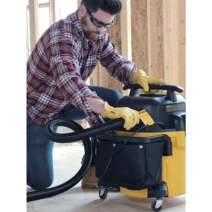 DeWalt Elektro-Nass- & Trockensauger DXV20P - 1.050 W, Behältervolumen: 20 l, Vollautomatisch - Der gelbe DeWalt Nass- und Trockensauger in Aktion, mit einem Handwerker, der den Schlauch anschließt. Er ist ein robustes Reinigungsgerät.