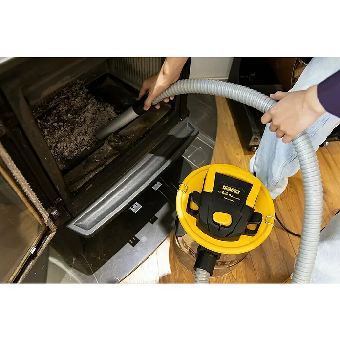 DeWalt Elektro-Aschesauger DXV15A - 600 W, Behältervolumen: 15 l, Mit Beutel - Eine Person reinigt einen Kaminofen mit einem gelben DeWalt Aschesauger, um die Asche effektiv zu entfernen.