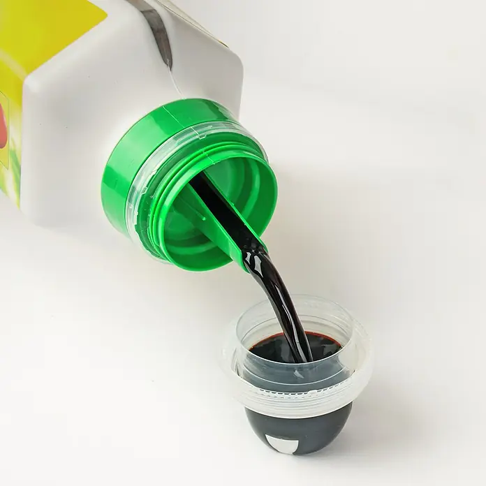Compo Rasendünger Unkraut & Moos Nein Danke - 1,3 l - Dunkle Flüssigkeit wird aus einer Flasche mit grünem Deckel in einen Messbecher gegossen.