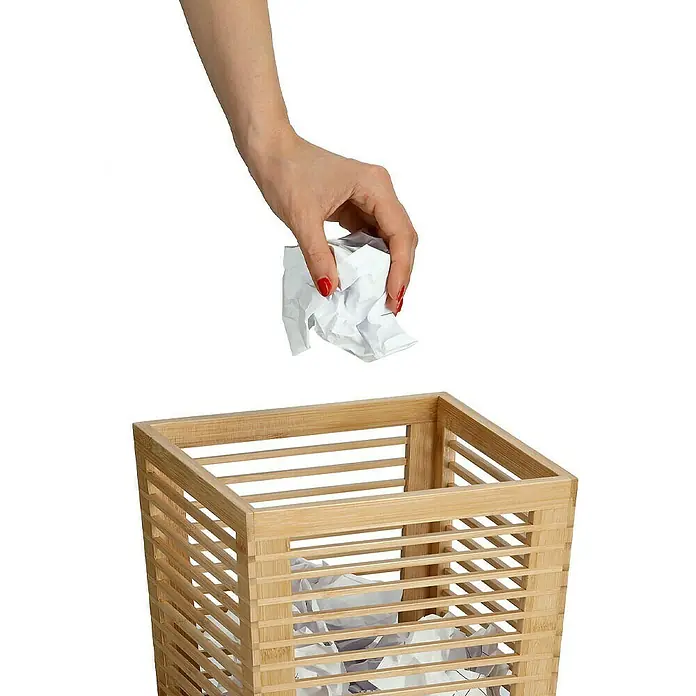 Zeller Present Papierkorb - 23,5 x 23,5 x 33 cm, Bambus, Natur - Ein offener quadratischer Papierkorb aus Holzlatten mit einer Hand, die zerknittertes Papier hineinwirft.