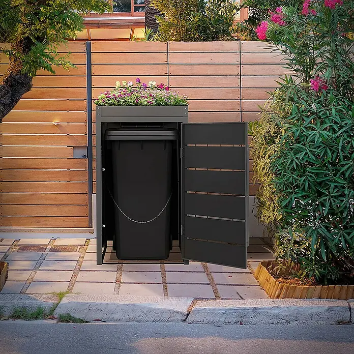 ML-Design Mülltonnenbox 1er 240L mit Pflanzdach und Magnetverschluss 68x80x124 cm Anthrazit - Stahl, Anthrazit, Geeignet für Anzahl Mülltonnen: 1 Stk. - Das Bild zeigt eine graue Mülltonnenbox mit Blumenkasten auf einem gepflasterten Weg neben einer Holzwand und Büschen.