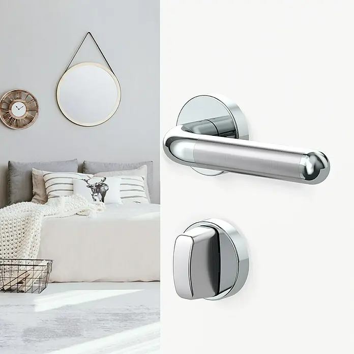 Diamond Doors Creative Drückergarnitur WC Idaho - Schlitzkopf/Olive - Nahaufnahme eines modernen Türgriffs aus Edelstahl mit Rosette und WC-Schloss vor einem Schlafzimmerhintergrund.