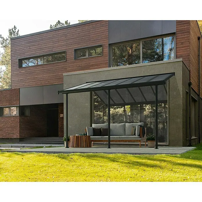 Palram – Canopia Terrassenüberdachung Sierra - B x T: 434 x 299 cm, Anthrazitgrau, Polycarbonat, Klar - Bild einer modernen Terrassenüberdachung mit Sofa und Tisch. Die Überdachung bietet Schutz und Stil für den Außenbereich.