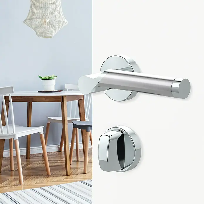 Diamond Doors Creative Drückergarnitur WC Alabama - Edelstahl, Schlitzkopf/Olive - Nahaufnahme eines modernen Türgriffs aus poliertem Chrom auf einer weißen Tür vor einem Esszimmer.