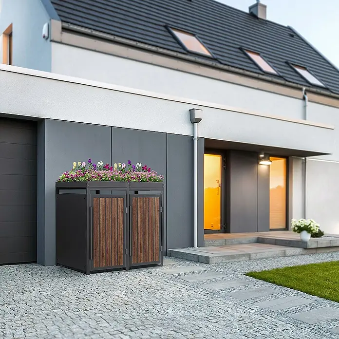 ML-Design Mülltonnenbox Mülltonnencontainer mit Pflanzdach für 2 Tonnen 120 oder 240 Liter - Stahl, Eiche dunkel, Geeignet für Anzahl Mülltonnen: 3 Stk. - Eine elegante Mülltonnenbox mit Holztüren und integriertem Pflanzkasten, der mit bunten Blumen bepflanzt ist, vor einem modernen Haus.
