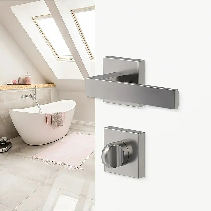 Diamond Doors Creative Zimmertürgarnitur WC Savannah - Stärke Tür: 40 mm - 45 mm, Samtgrau, Schlitzkopf/Olive - Nahaufnahme eines modernen Türgriffs aus Edelstahl mit quadratischer Rosette und Hebel vor einem Badezimmerhintergrund.