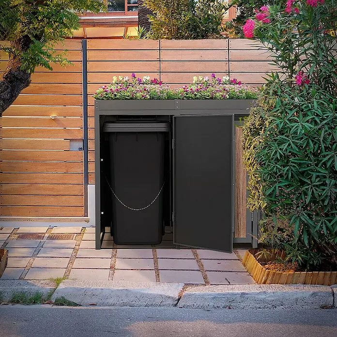 ML-Design Mülltonnenbox Mülltonnencontainer mit Pflanzdach für 4 Tonnen 120 oder 240 Liter - Stahl, Eiche dunkel, Geeignet für Anzahl Mülltonnen: 4 Stk. - Eine Mülltonnenbox mit Pflanzkasten auf Pflastersteinen, die eine schwarze Mülltonne verbirgt und mit bunten Blumen bepflanzt ist.