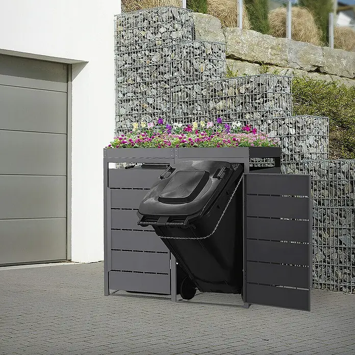 ML-Design Mülltonnenbox Mülltonnencontainer mit Pflanzdach für 2 Tonnen 120 oder 240 Liter - 80 x 80 cm, Stahl, Anthrazit, Geeignet für Anzahl Mülltonnen: 2 Stk. - Mülltonnenbox mit Bepflanzung auf einem gepflasterten Hof, neben einer Garage und einem Gabionenzaun.