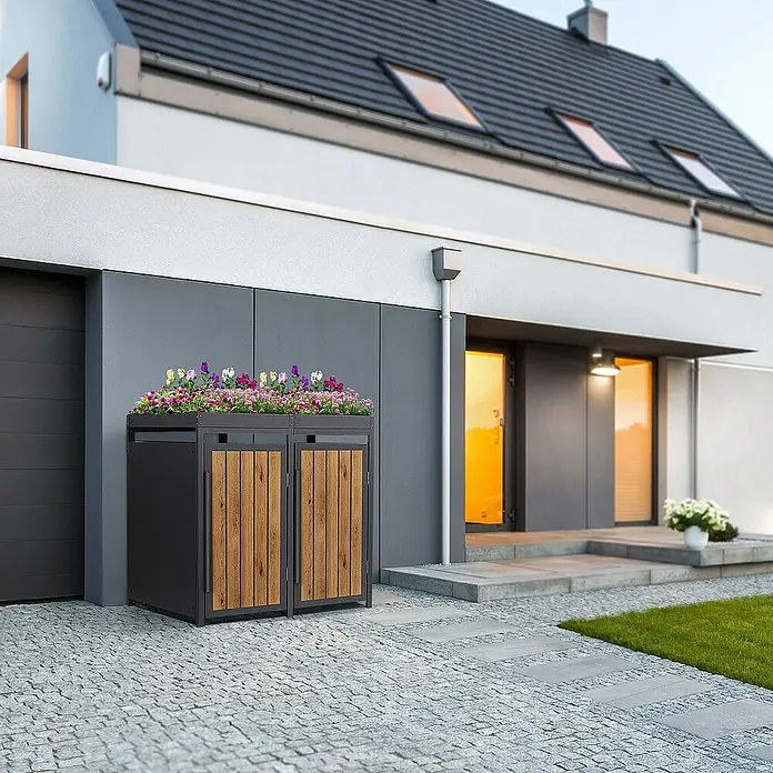 ML-Design Mülltonnenbox Mülltonnencontainer mit Pflanzdach für 2 Tonnen 120 oder 240 Liter - Stahl, Eiche hell, Geeignet für Anzahl Mülltonnen: 2 Stk. - Ein Mülltonnenbox mit Pflanzkasten obenauf, auf einer gepflasterten Auffahrt vor einem modernen Haus.