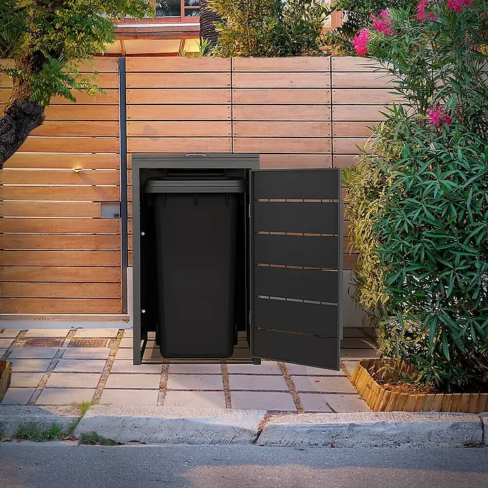 ML-Design Mülltonnenbox Mülltonnencontainer mit Klappdeckel/Tür für 1 Tonne 120 oder 240 Liter - Stahl, Anthrazit, Geeignet für Anzahl Mülltonnen: 1 Stk. - Ein Mülltonnenbox aus Metall mit einer schwarzen Mülltonne darin, die vor einer Holzwand auf Pflastersteinen steht.