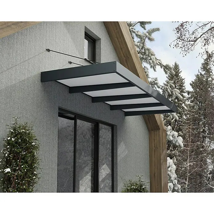 Palram – Canopia Pultvordach Sophia XL - 379 x 140 x 17 cm, Anthrazitgrau, Farbe Dach: Opal - Nahaufnahme einer modernen Haustürüberdachung mit grauen Rahmen und weißen Paneelen an einem Haus mit Winterlandschaft im Hintergrund.