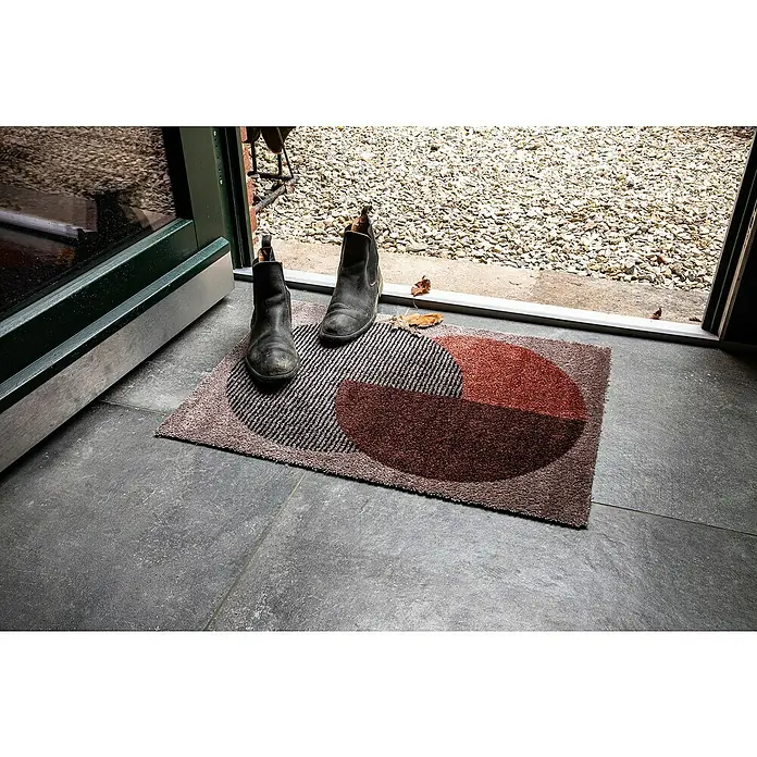 Fußmatte Manhatten - Beige/Terracotta, 70 x 50 cm, 100 % Polyamid - Diese Aufnahme zeigt eine Fußmatte mit grafischem Muster und ein Paar schwarze Stiefel vor einer offenen Tür.