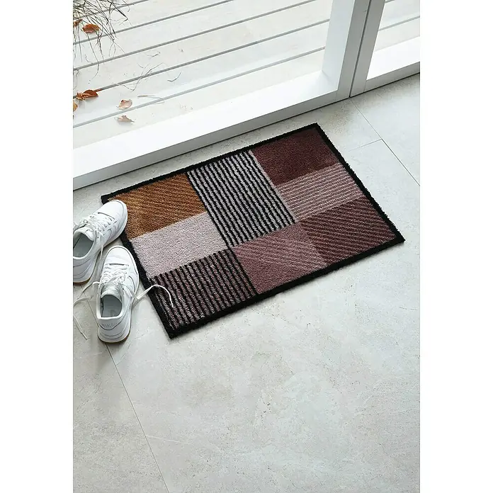 Fußmatte Manhatten - Geomix Kastanie/Rose, 100 x 67 cm, 100 % Polyamid - Nahaufnahme einer rechteckigen, mehrfarbigen Fußmatte mit geometrischen Mustern und einem Paar weißer Turnschuhe daneben.