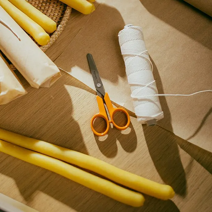 Fiskars Schere Classic - Länge: 13 cm, Orange - Handgefertigte Kerzenherstellung mit gelben Kerzen, Schere und einer Rolle weißen Fadens auf einem Holztisch.