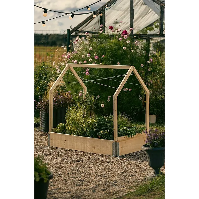 Upyard Hochbeet-Überdachung Schutzrahmen inkl. 3 Abdeckungen - Passend für: Hochbeete 120 × 80 cm - Ein erhöhter Gartenkasten aus Holz mit Hausrahmen und Pflanzen darin, umgeben von Blumen und Kies. Lichterketten im Hintergrund.