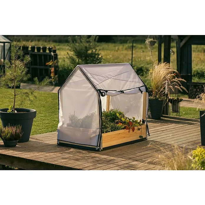 Upyard Hochbeet-Überdachung Schutzrahmen inkl. 3 Abdeckungen - Passend für: Hochbeete 120 × 80 cm - Nahaufnahme eines Mini-Gewächshauses aus Holz und transparenter Plane auf einer Holzterrasse, umgeben von Pflanzen.