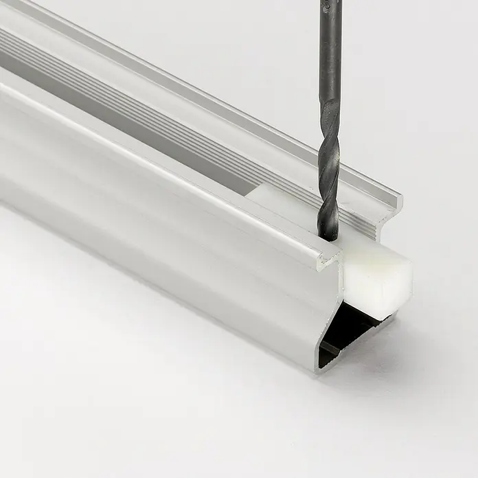 Room Plaza Easy Schiebetür-Bau-Set - Eiche Country/Pinie White, Farbe Beschlag: Silber - Eine Nahaufnahme eines Bohrers, der in ein Aluminiumprofil mit einem weißen Kunststoffeinsatz bohrt. Das Bild zeigt die Präzision des Werkzeugs.