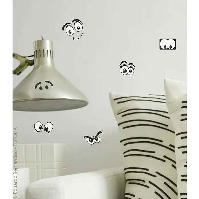 Vinilo de pared - Ojos cómicos, Negro, Plástico - Adhesivos de pared con varios diseños de ojos de dibujos animados que adornan una pared blanca sobre una lámpara y cojines.