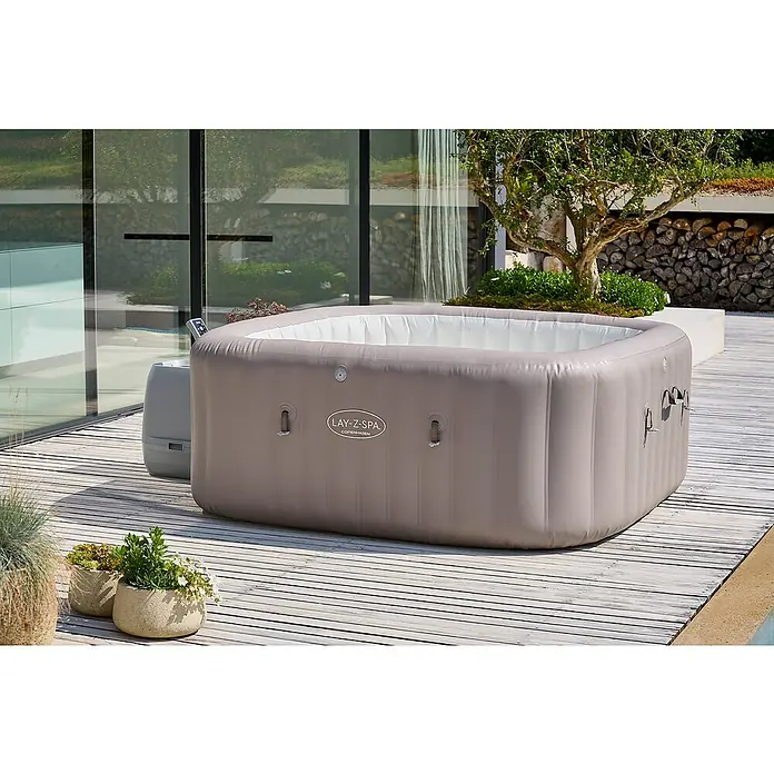 Bestway Lay-Z-Spa Mobil-Whirlpool Copenhagen Hydrojet - L x B x H: 201 x 201 x 80 cm, Grau, 1.050 l - Ein Lay-Z-Spa Whirlpool im Außenbereich auf einer Terrasse, umgeben von Pflanzen und moderner Architektur. Ideal zur Entspannung im Garten.
