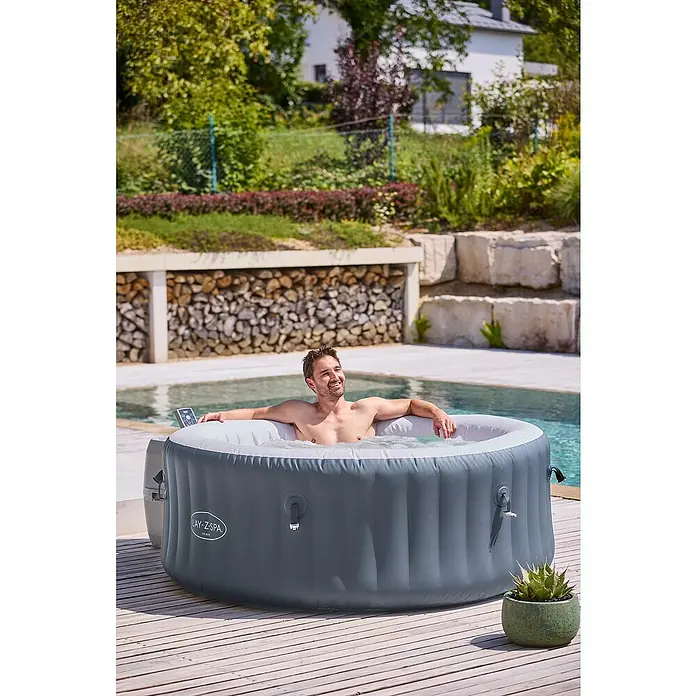 Bestway Lay-Z-Spa Mobil-Whirlpool Miami Air-Jet - Ø x H: 180 x 66 cm, Anthrazit, 669 l - Ein Mann entspannt in einem Lay-Z-Spa Whirlpool im Freien, umgeben von Grün. Der graue Whirlpool bietet Entspannung und Komfort.