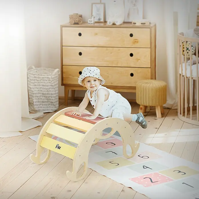 ECD Germany Klettergerüst Kletterbogen trainiert Gleichgewicht & Balance ab 2 Jahren - 74 x 41 x 38,5 cm, Holz, Mehrfarbig - Ein kleines Kind klettert auf einer farbenfrohen Kletterwippe in einem hellen Kinderzimmer. Im Hintergrund sind Möbel und Spielsachen sichtbar.
