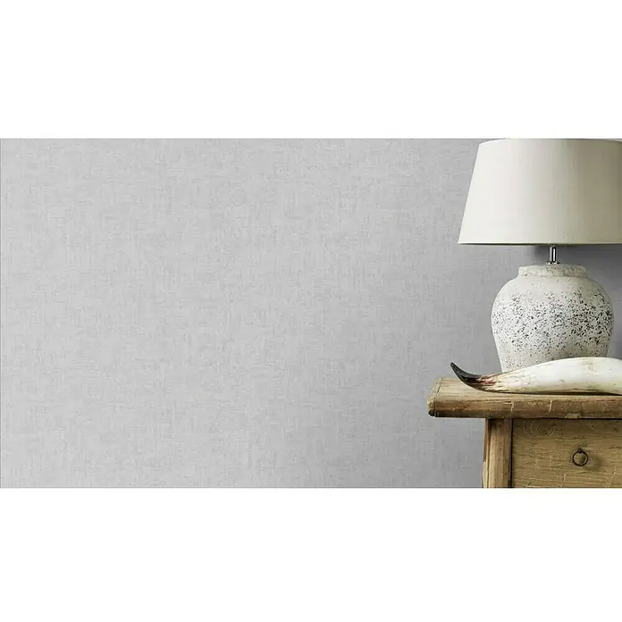 Rasch Vliestapete - Grau, Uni, 10,05 x 0,53 m, Schimmernd - Elegante Tischleuchte mit beigem Lampenschirm und dekorativem Horn auf einem rustikalen Holztisch, vor einer dezenten, strukturierten Wand.
