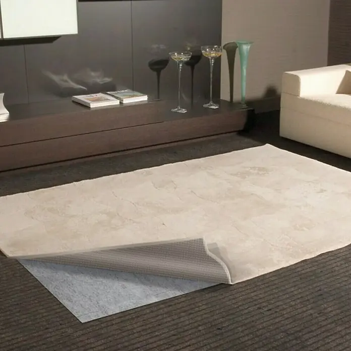 D-c-fix Teppichgleitschutz Trent - 120 x 60 cm, Selbstklebend - Ein cremefarbener Teppich mit hochgeklappter Ecke, der die graue Unterseite zeigt, liegt in einem Wohnzimmer.