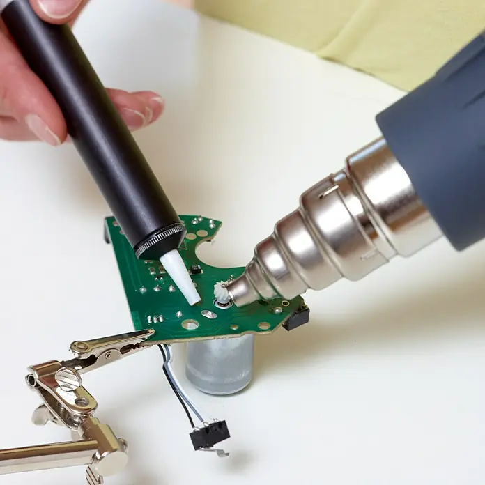Rapid Reduzierdüse - Durchmesser: 9 mm, Passend für: Heißluftgebläse - Ein Bild von Reparaturarbeiten an einer Platine mit Heißluftpistole und Lötzinn, wobei die Elektronik im Fokus steht.