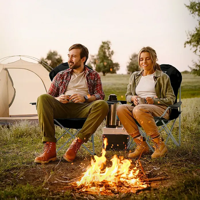 Hauki Campingstuhl Faltstühl faltbar mit Getränkehalter & Tragetasche bis 150kg - Stahl, Polyester, Klappbar, Schwarz, B x T x H: 56 x 56 x 110 cm - Ein Paar entspannt in Campingstühlen am Lagerfeuer, mit Zelt im Hintergrund.