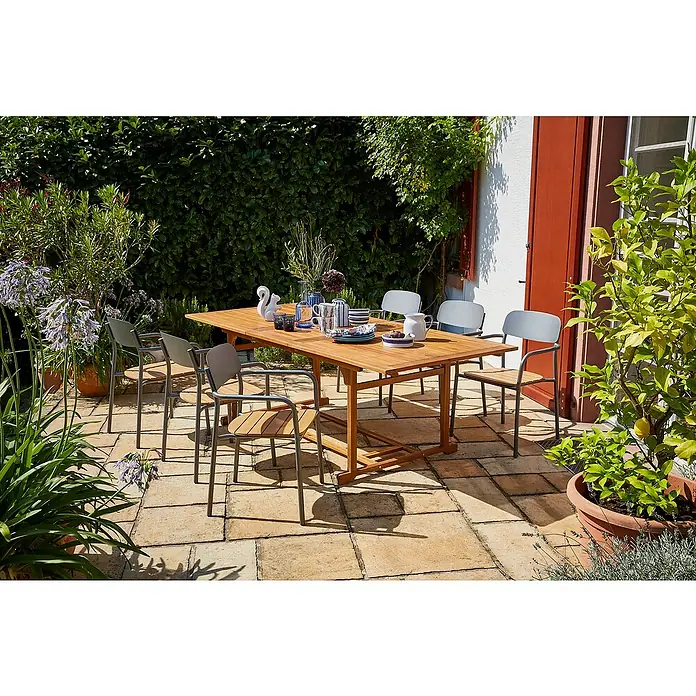 Sunfun Gartenmöbel-Set Diana/Gastro - 7 -tlg., Akazie, Stahl, Polywood, Naturbraun/Night-Grey - Einladender Gartentisch mit Stühlen auf einer sonnigen Terrasse, gedeckt mit Geschirr, umgeben von üppigem Grün.