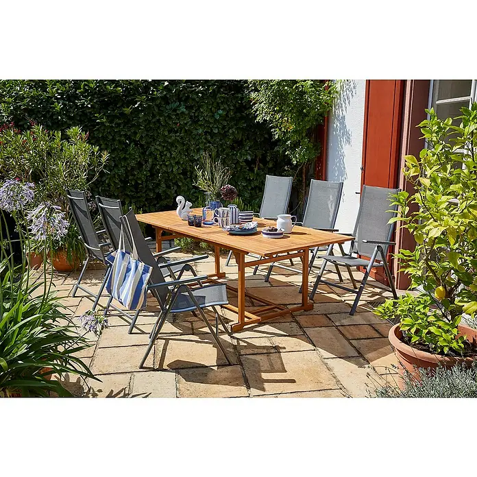 Sunfun Gartenmöbel-Set Diana/Maja - 7 -tlg., Akazie, Aluminium, Textilen, Naturbraun/Anthrazit - Ein Gartentisch mit Stühlen auf einer Terrasse, umgeben von üppigem Grün und Pflanzen in Töpfen für einen entspannten Außenbereich.