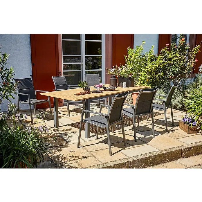 Sunfun Gartenmöbel-Set Carina/Maja - 7 -tlg., Aluminium, Akazie, Stahl, Textilen, Grau/Hellbraun - Ein Gartentisch mit sechs Stühlen auf einer Terrasse, umgeben von Pflanzen. Das Möbel-Set lädt zum Verweilen im Freien ein.