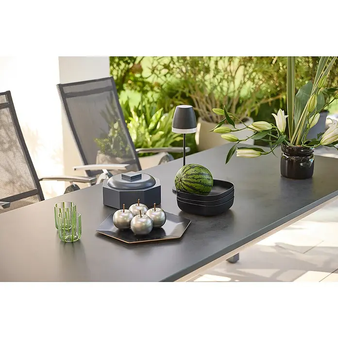 Sunfun Maja Gartentisch - L x B x H: 220 x 90 x 74 cm, Aluminium, Glas, Night-Grey - Ein stilvoller Tisch mit Dekorationsartikeln wie einer Lampe, Obstschale und Blumen, der eine einladende Atmosphäre schafft.
