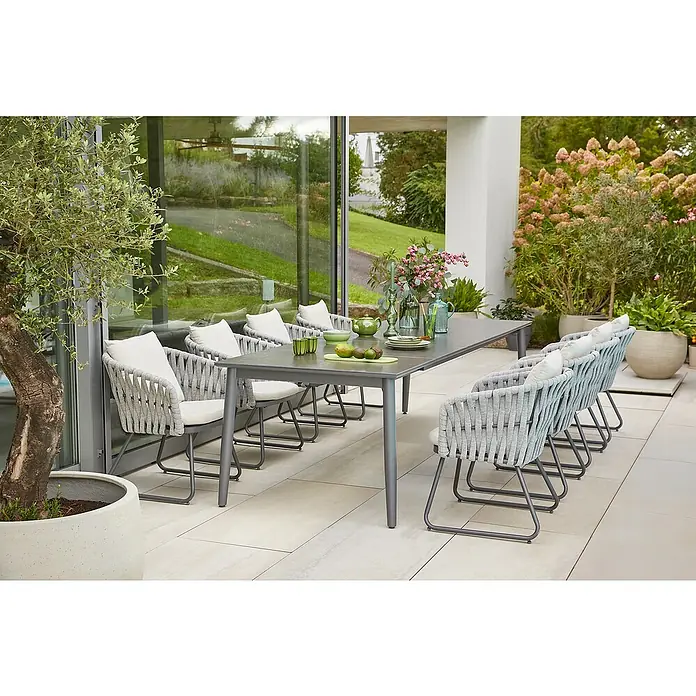 Sunfun Gartenmöbel-Set Solo/Maja Rope - 9 -tlg., Aluminium, Sintered Stone, Seilgeflecht, Polyester, Grau/Weiß/Night-Grey - Einladende Gartensitzgruppe mit grauem Tisch und geflochtenen Stühlen mit hellen Kissen auf einer Terrasse.