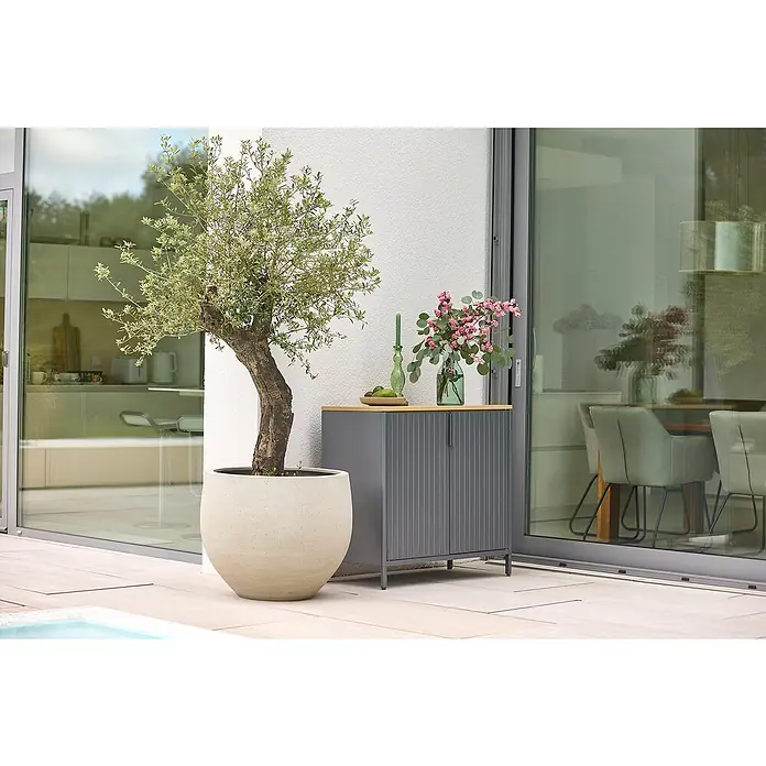 Sunfun Solo Garten-Aufbewahrungschrank - L x B x H: 90 x 46 x 86 cm, Stahl, Polywood, Night-Grey - Ein grauer Terrassenschrank mit einer Holzplatte, dekoriert mit Blumen und einer Kerze, neben einem Olivenbaum im Topf.