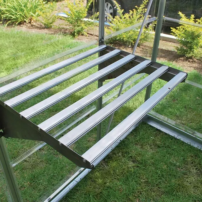 Palram – Canopia Gewächshaus-Einlegeboden Heavy Duty - 58 x 42 x 22 cm, 1 Stk. - Nahaufnahme eines silbernen Gewächshausregals mit Lattenrost vor einem Hintergrund aus grünem Gras und Pflanzen.
