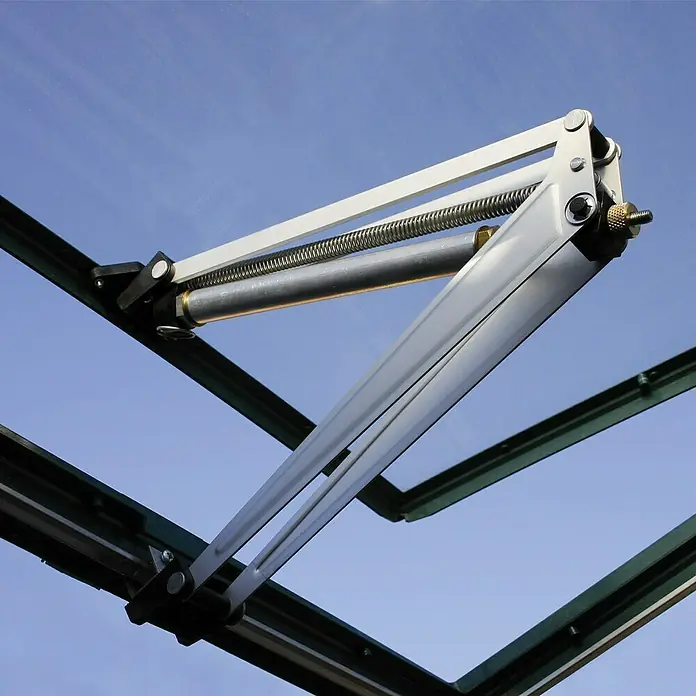 Palram – Canopia Automatischer Fensteröffner - Passend für: Palram Gewächshäuser - Nahaufnahme eines Gewächshausfensteröffners mit Zylinder und Feder, montiert an einem grünen Rahmen unter blauem Himmel.