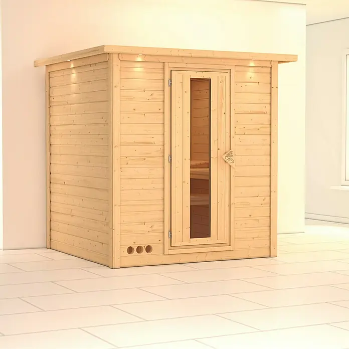 Karibu Elementsauna Mojave - Ohne Ofen, Mit Dachkranz und Beleuchtung, Materialspezifizierung Tür: Massivholztür, L x B x H: 224 x 210 x 192 cm - Sauna mit Holztür und Beleuchtung in einem hellen Raum.