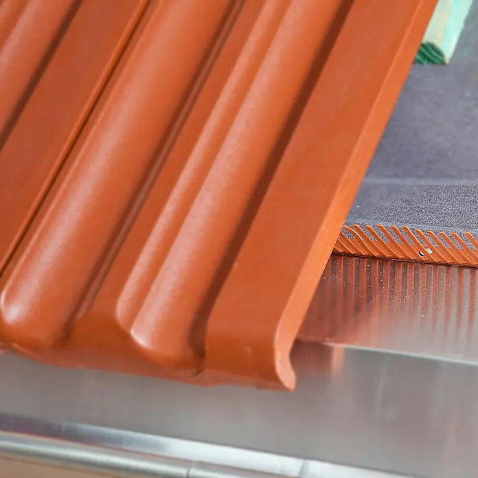 Sarei Traufenkamm - 100 x 5,5 x 1 cm, Ziegelrot - Nahaufnahme von braunen Dachziegeln auf einem glänzenden Metalldach. Detailaufnahme der Installation von Dachelementen für Neubau oder Sanierung.