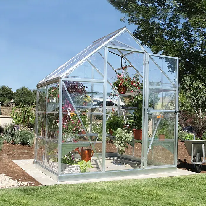 Palram – Canopia Invernadero Harmony - Medidas ext. (An x Pr): 185 x 126 cm, Plateado, Área: 2,3 m² - Amplio invernadero de vidrio y metal lleno de plantas y suministros de jardinería en un jardín verde.