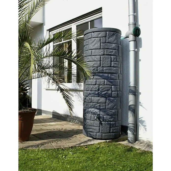 Arves Regenspeicher Arcado - 460 l, Black Granitfarben - Eine Regentonne in Steinoptik steht neben einem Fallrohr an einer weißen Hauswand, ideal zur Gartenbewässerung.