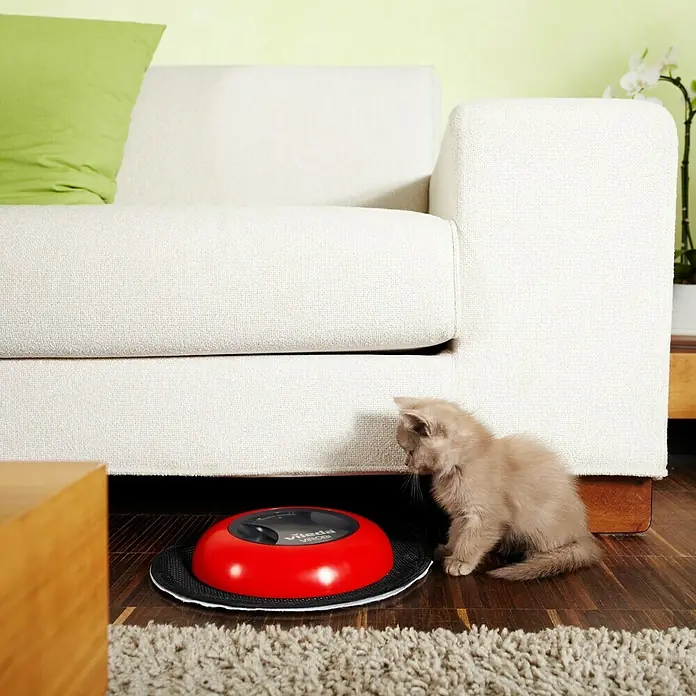 Vileda ViROBi Saugroboter Slim - Schwarz/Rot, Akkulaufzeit: 240 min, Li-Ionen - Ein roter Vileda Saugroboter wird von einer neugierigen Katze unter einem Sofa erkundet. Das Gerät reinigt den Boden selbstständig.