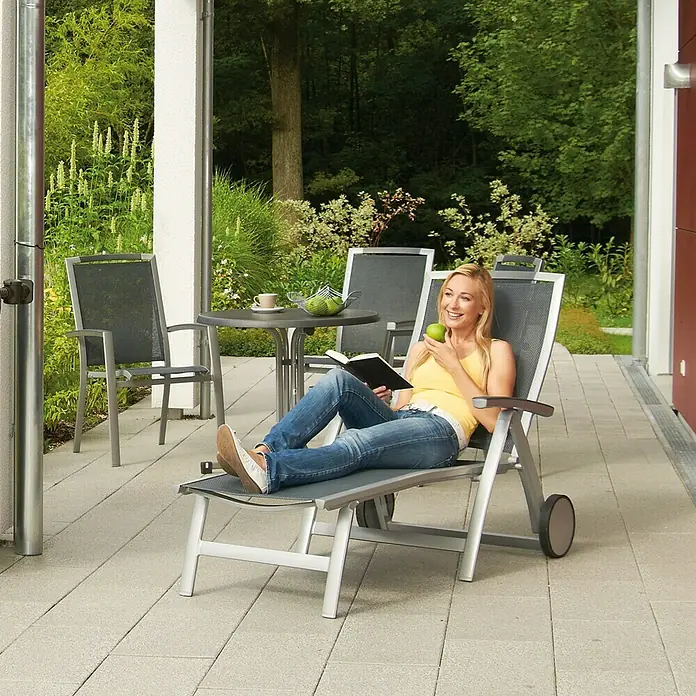 Garantia Exklusive Line Regenspeicher Amphore - 360 l, Darkgranite - Frau entspannt auf einer grauen Gartenliege mit Rollen, liest ein Buch und isst einen Apfel auf einer Terrasse.