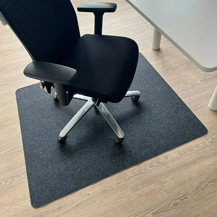Fußbodenschutzmatte Viking - 120 x 100 cm, Dunkelgrau, Polyester - Bürostuhl auf dunkelgrauer Stuhlunterlage auf hellem Holzboden. Ein Tisch ist ebenfalls sichtbar.