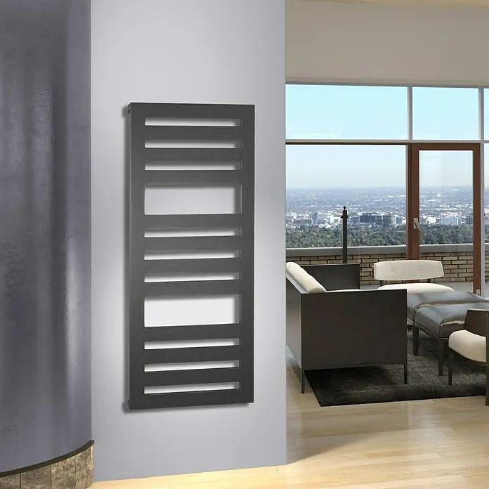 Szagato Designheizkörper Zebra 2 - B x H: 600 x 1.440 mm, Wärmeleistung bei Vorlauftemperatur von 75 °C (D: 50): 911 W, Moonstone-Grau - Ein grauer Design-Heizkörper mit horizontalen Schlitzen hängt an einer weißen Wand in einem stilvollen Raum mit großer Fensterfront.