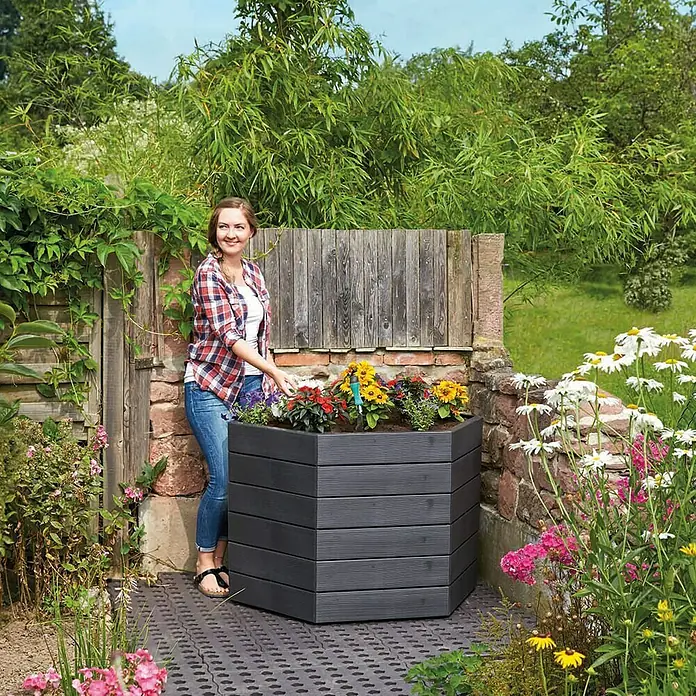 Garantia Hochbeet Ergo Wood - Ø x H: 110 x 25 cm, Kunststoff, Anthrazit - Frau gießt Blumen in einem sechseckigen, anthrazitfarbenen Hochbeet im Garten.